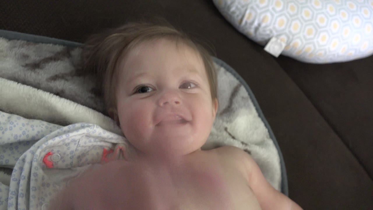 Toddler smiling slightly on a bed or couch.