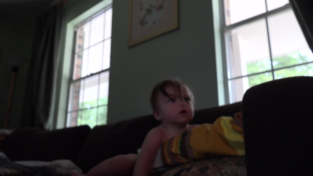 Infant on a couch in a dim living room beside an adult.