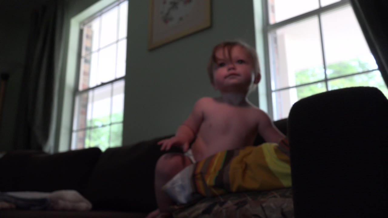 Toddler sitting on a couch near bright windows.