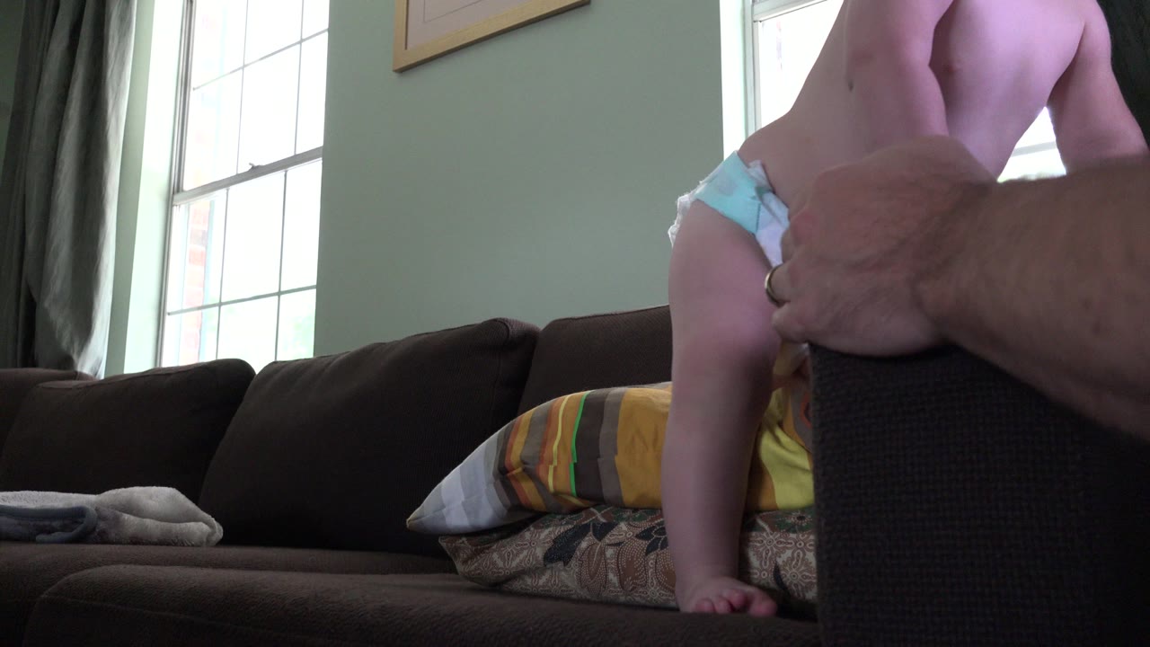 Toddler kneels higher on pillows with adult hand in front of the child.