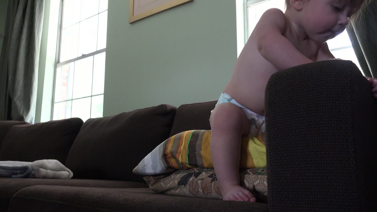 Baby climbing beside a dark sofa cushion in a living room.