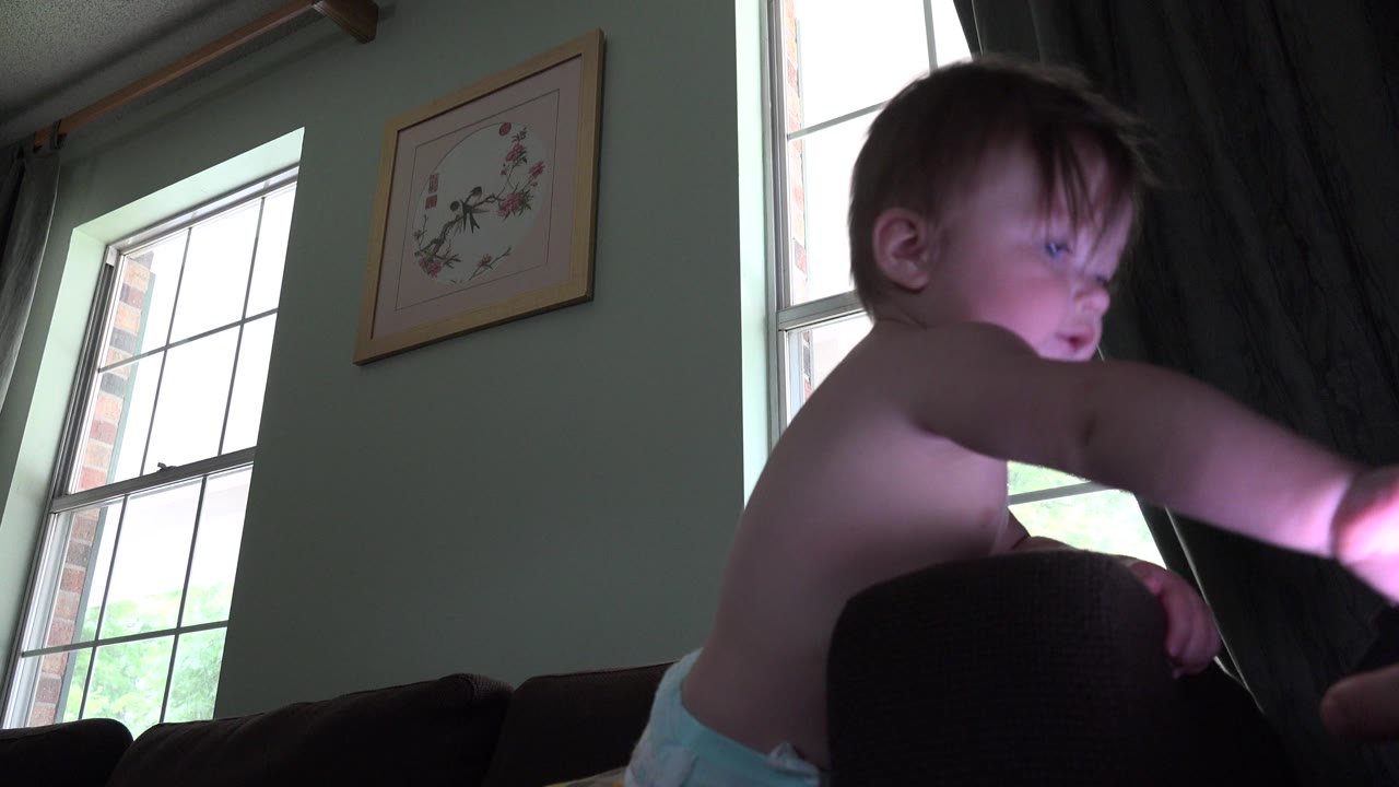 Toddler near a dark couch beside a curtained window.