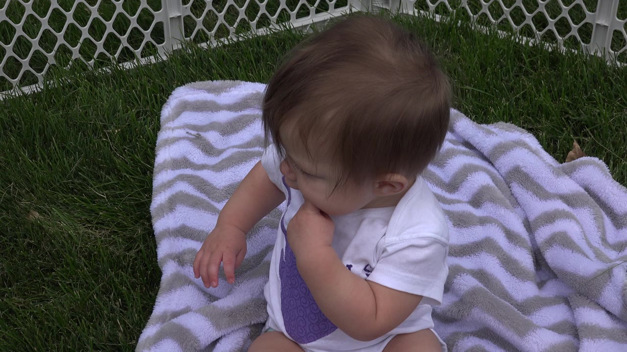 Baby sitting on a patterned blanket inside a white yard fence.