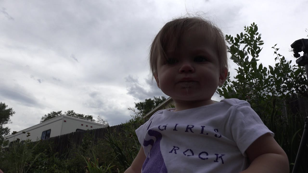 Young child close to a low outdoor camera under cloudy sky.