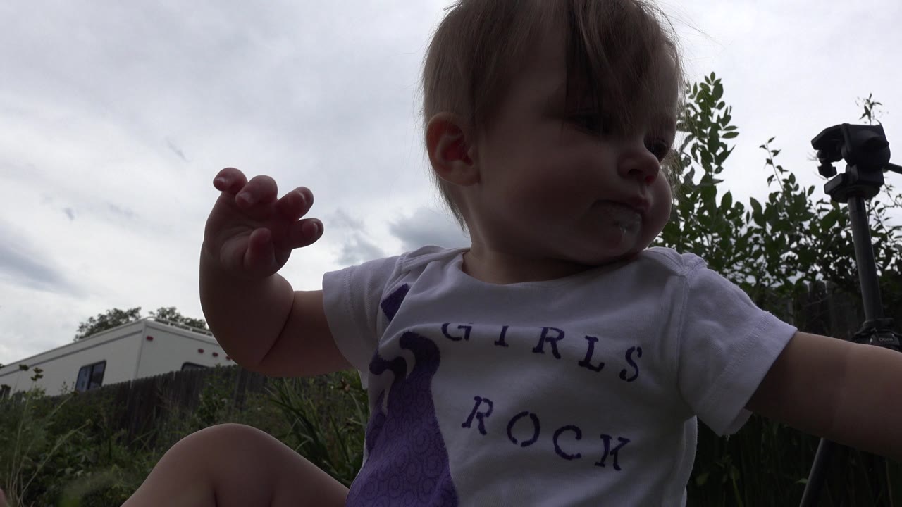 Blonde toddler sitting in grass under a cloudy sky.