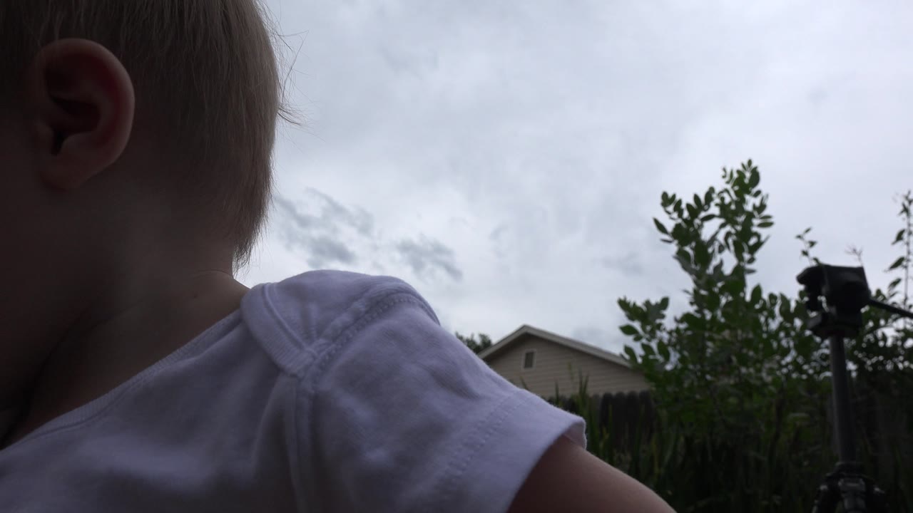 Baby shoulder and head close to camera against cloudy sky.