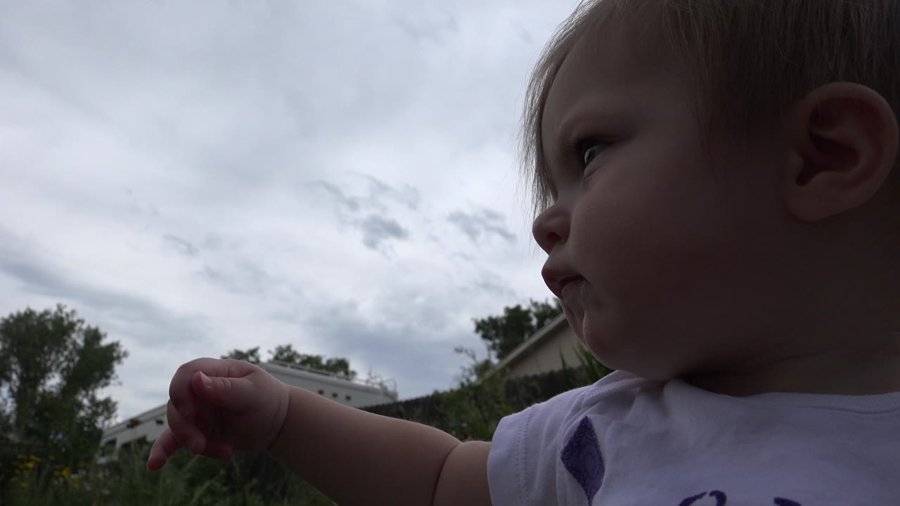 The baby remains in close side profile in Westminster, Colorado, with one arm raised and a dark, cloudy sky over trees and a fence in the background.