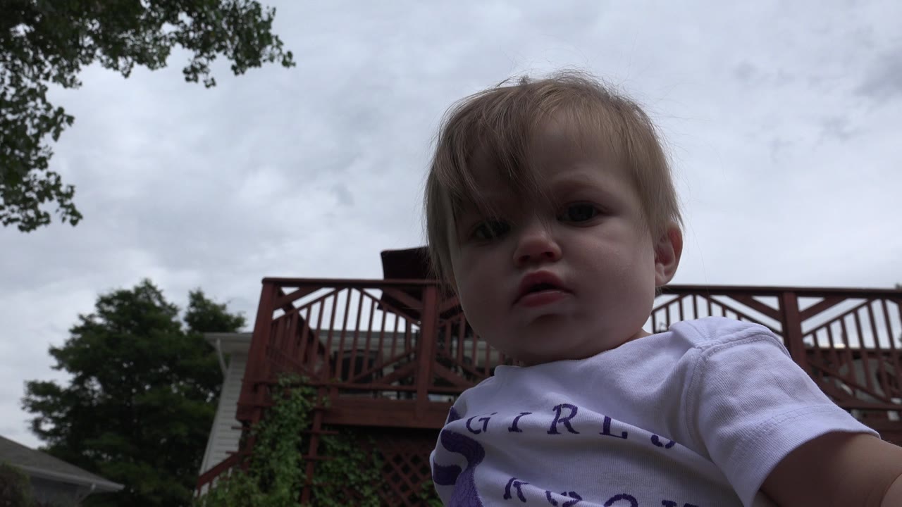 Young child close to a low camera under a cloudy sky.