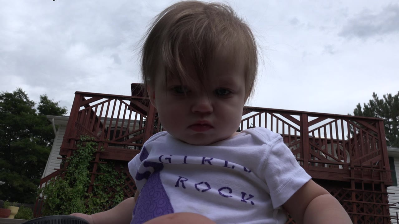Toddler close to camera with deck and cloudy sky behind.