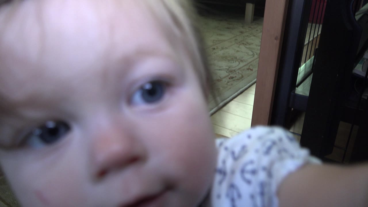 The toddler leans near the camera in Westminster, Colorado, with one eye and cheek prominent and the indoor rug and furniture softened in the background.