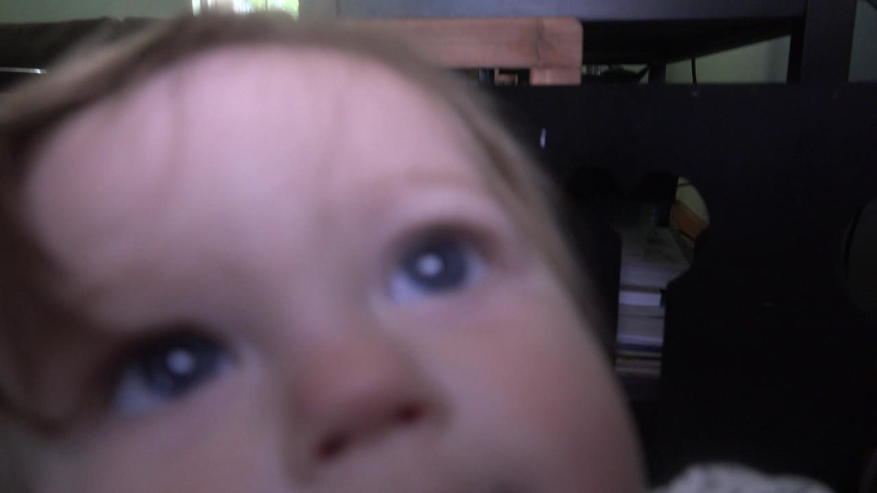 At 0:01 in Westminster, Colorado, the child's eyes are close to the lens while the TV stand, chair back, and dim living room background remain visible.