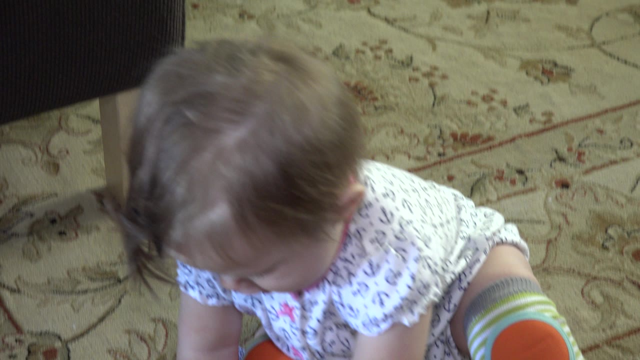 Baby looking down on a beige patterned carpet.