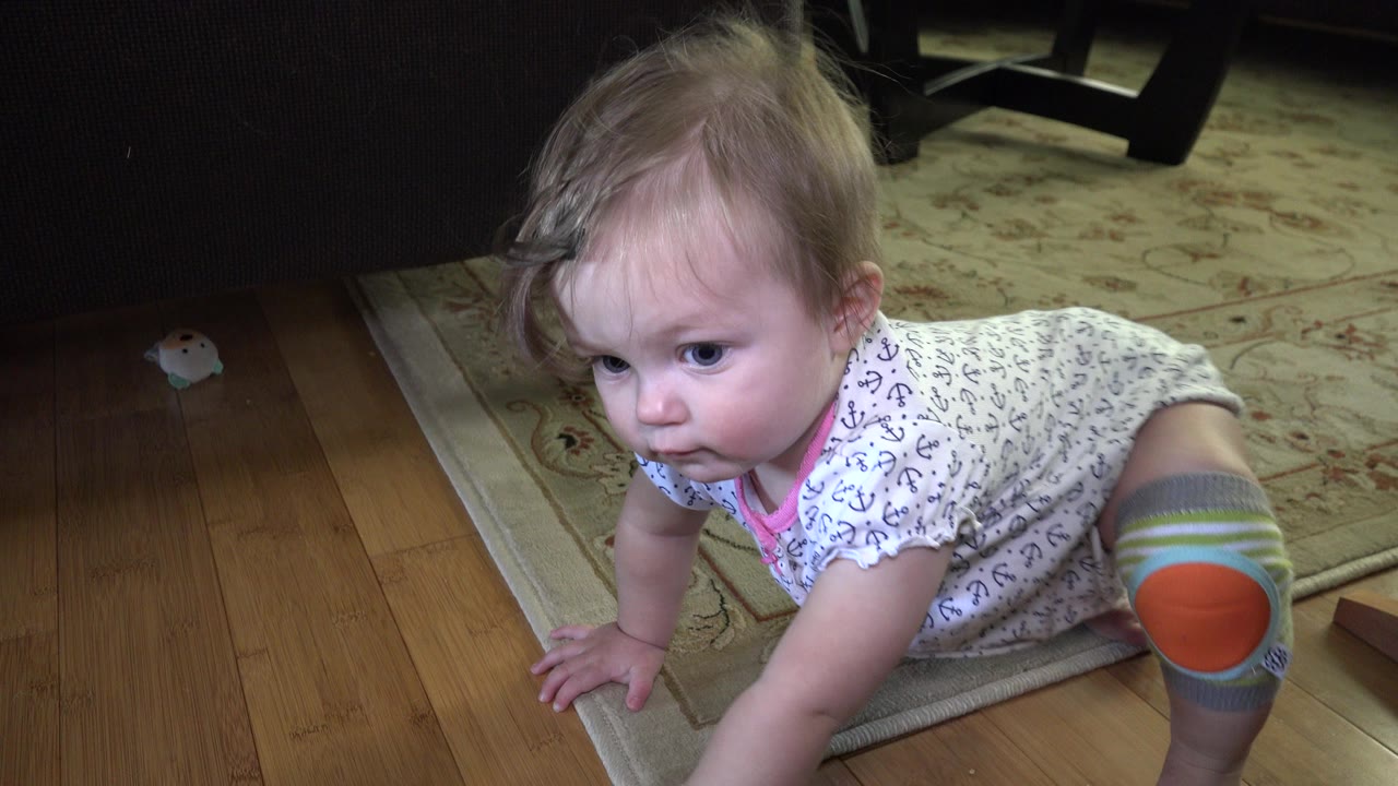 Baby crawling on a wood floor near a light rug.