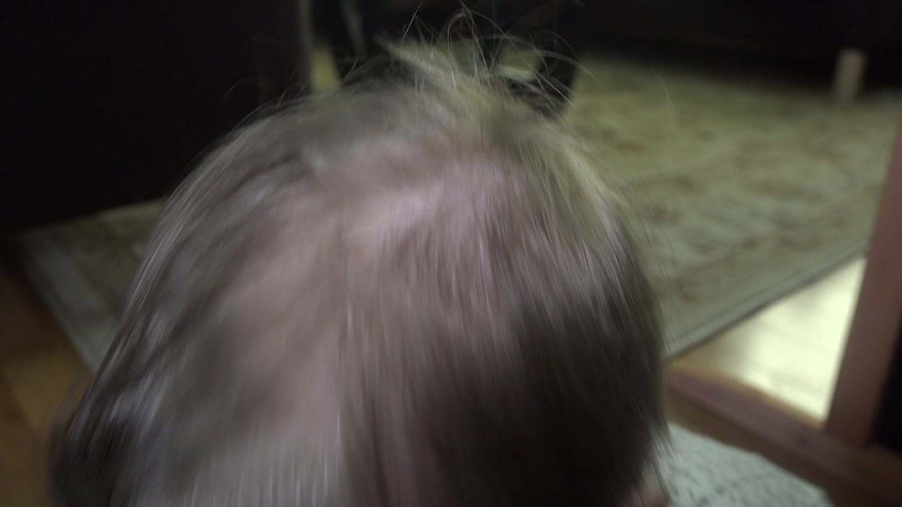 The child's hair remains close to the lens, with the patterned carpet and furniture legs visible behind it in the Westminster, Colorado interior.