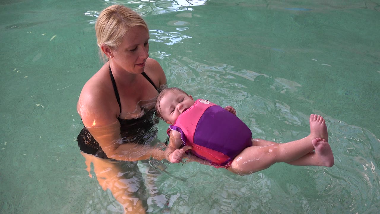 Mother holds baby floating in pool water.