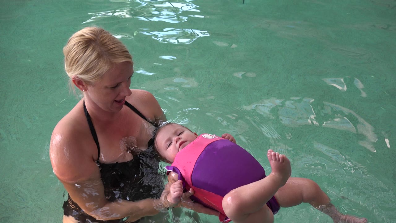 Mother supports baby floating on their back in a pool.