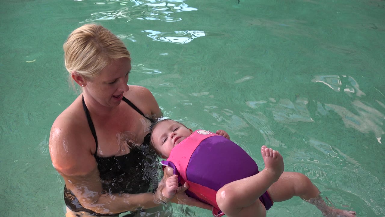 In Westminster, Colorado, the baby remains on their back near the mother's chest as the mother looks down and supports the flotation suit in the pool.