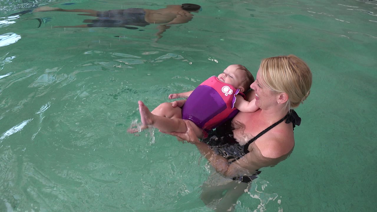 Mother holding a baby in a flotation vest in pool water.