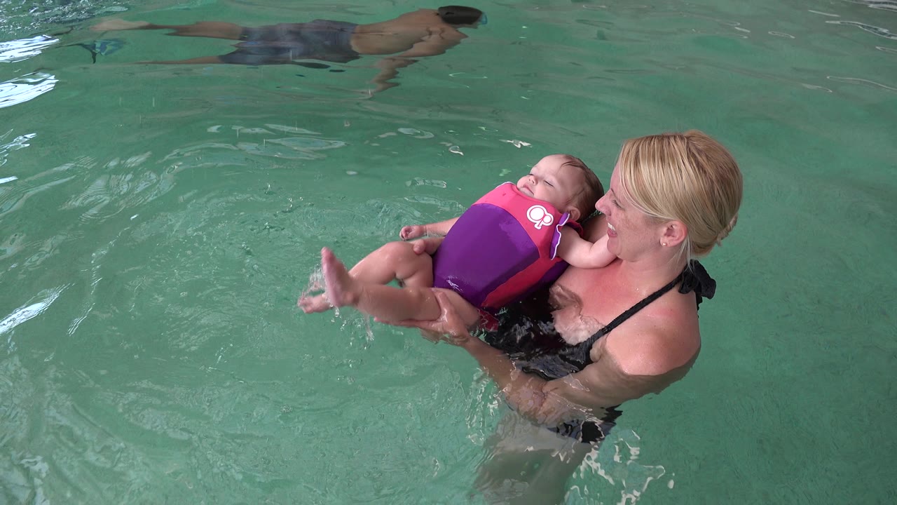In Westminster, Colorado, the mother keeps both hands under the baby while the child's legs extend outward and small ripples spread across the green pool water.