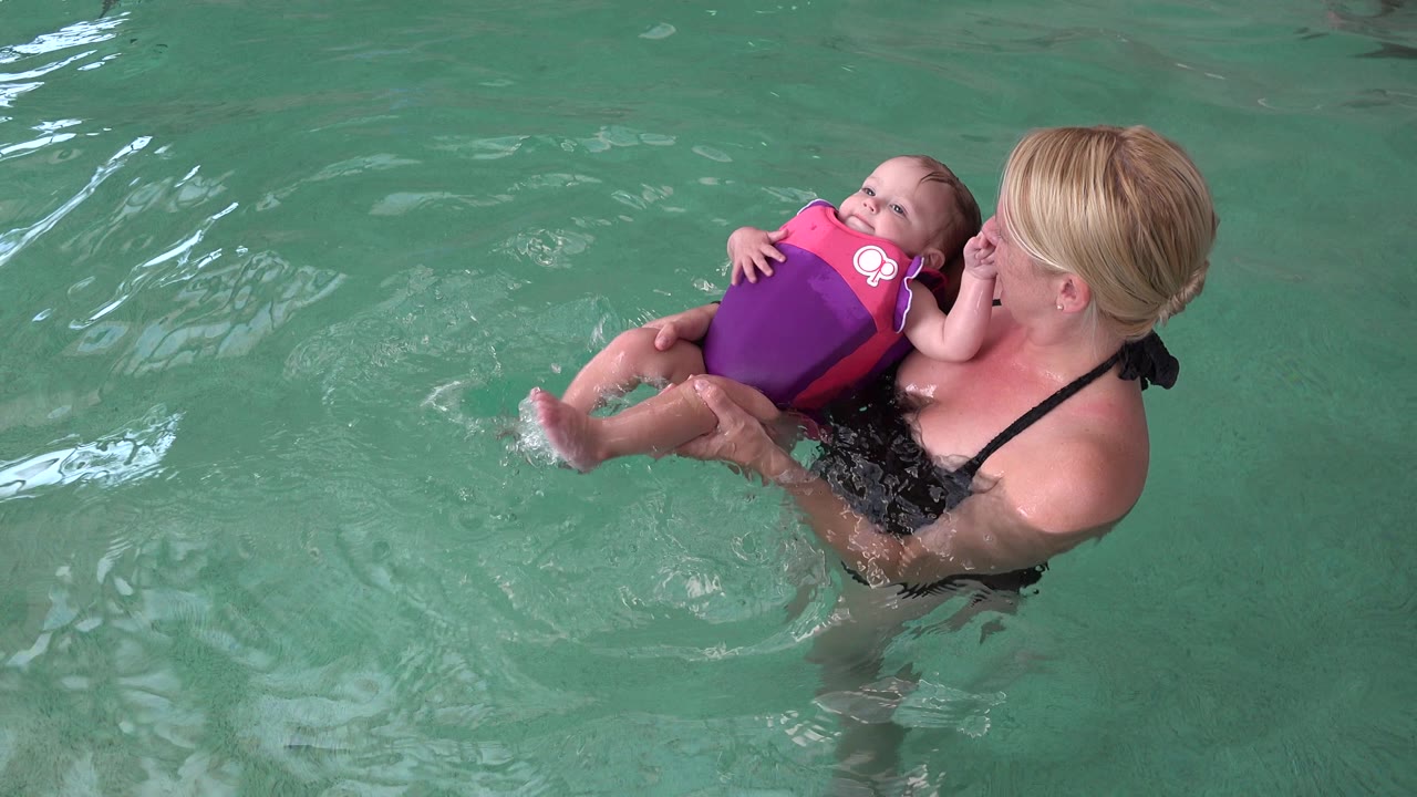 The baby leans back in the flotation vest while the mother holds them steady in rippling pool water in Westminster, Colorado.