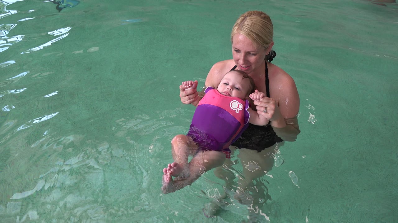 Baby in a life vest floating while a woman supports both hands.