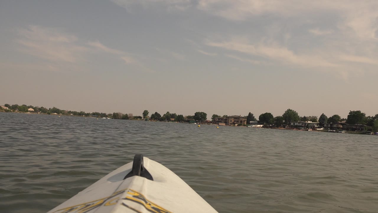 The kayak bow sits near the lower center as small waves cross Hidden Lake, Colorado, with trees and low buildings along the horizon, no visible people.
