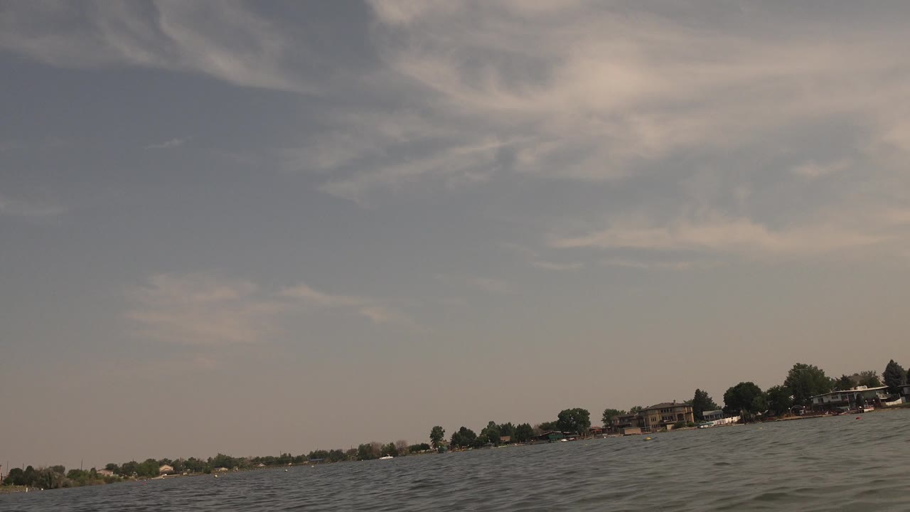 Choppy lake water with a distant tree-lined shoreline under hazy clouds.