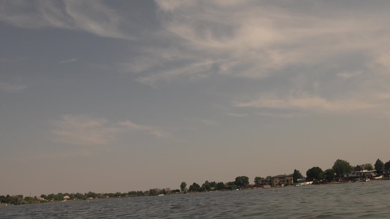 Second frame of Hidden Lake, Colorado showing a slightly tilted horizon, textured lake water, far shoreline trees and buildings, and no visible people.