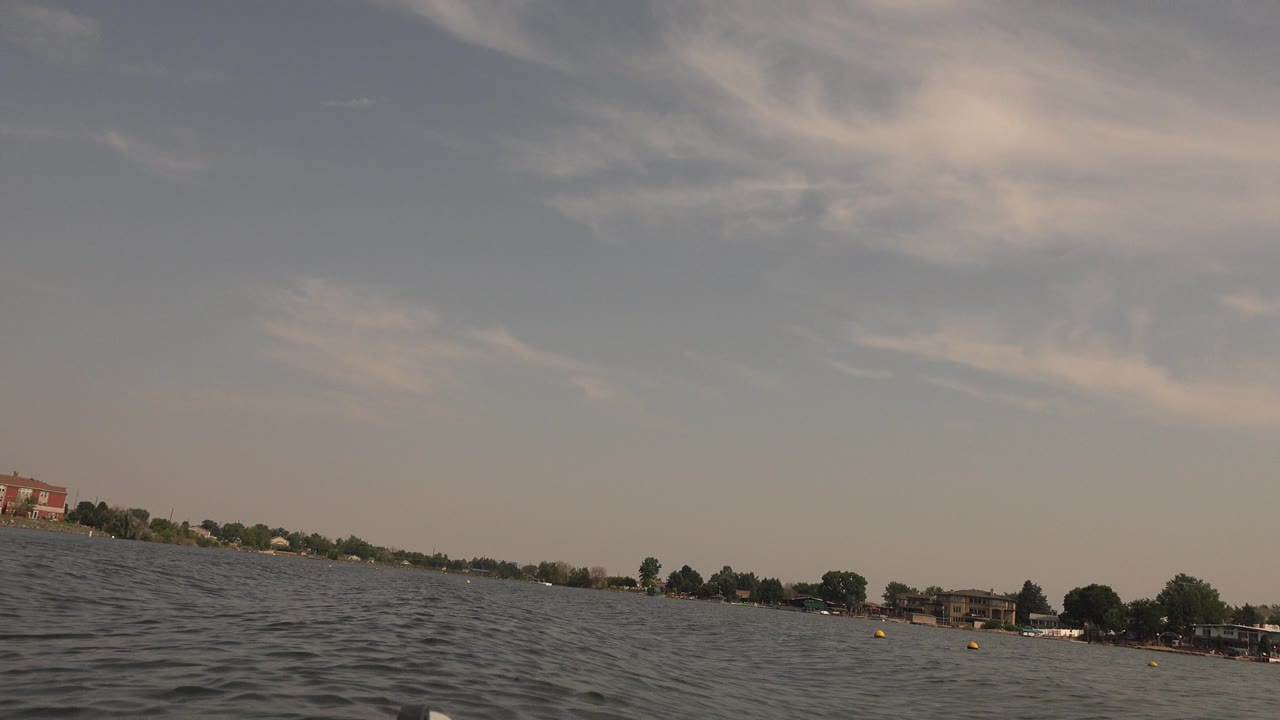 Low view across rippled lake water toward a distant shoreline and cloudy sky.