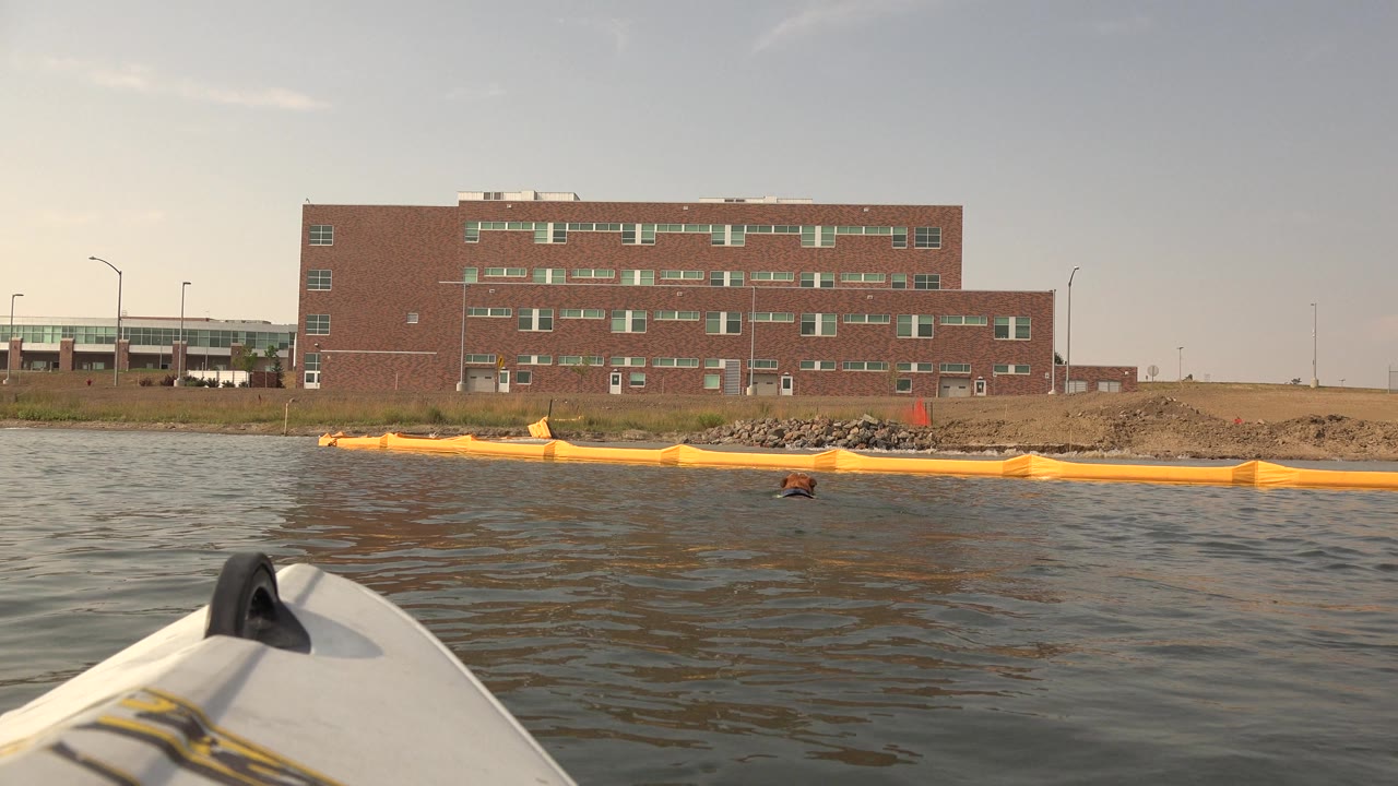 Low lake view with a white boat bow, yellow boom, and brick building.