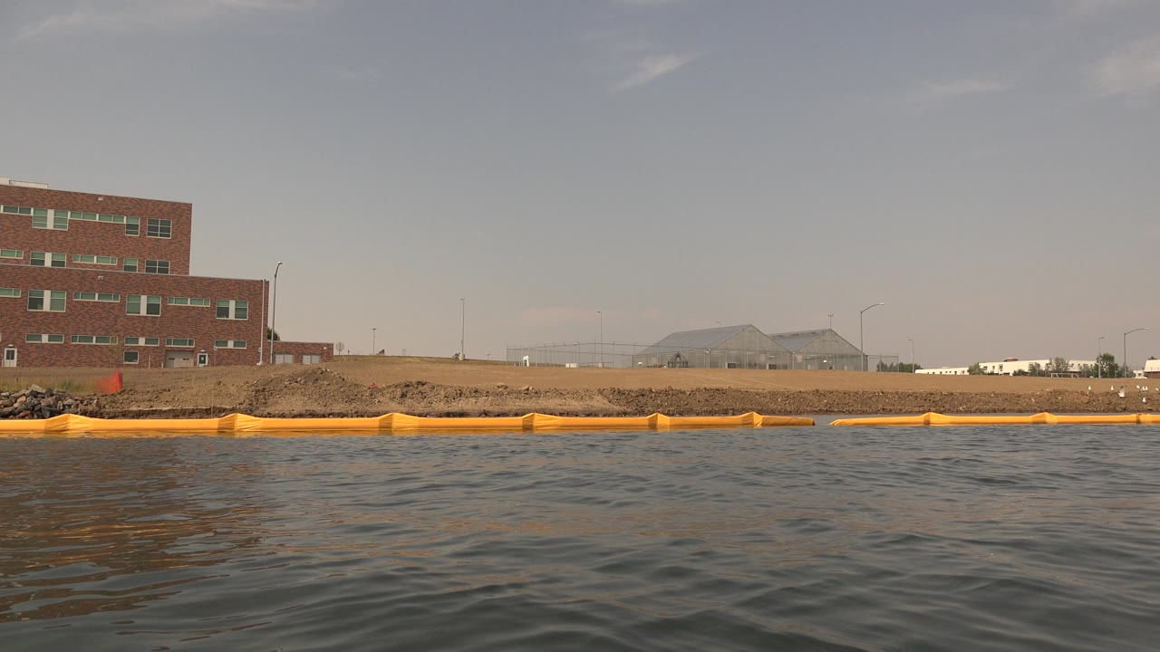 Wide lake shoreline with orange boom and brick building to the left.