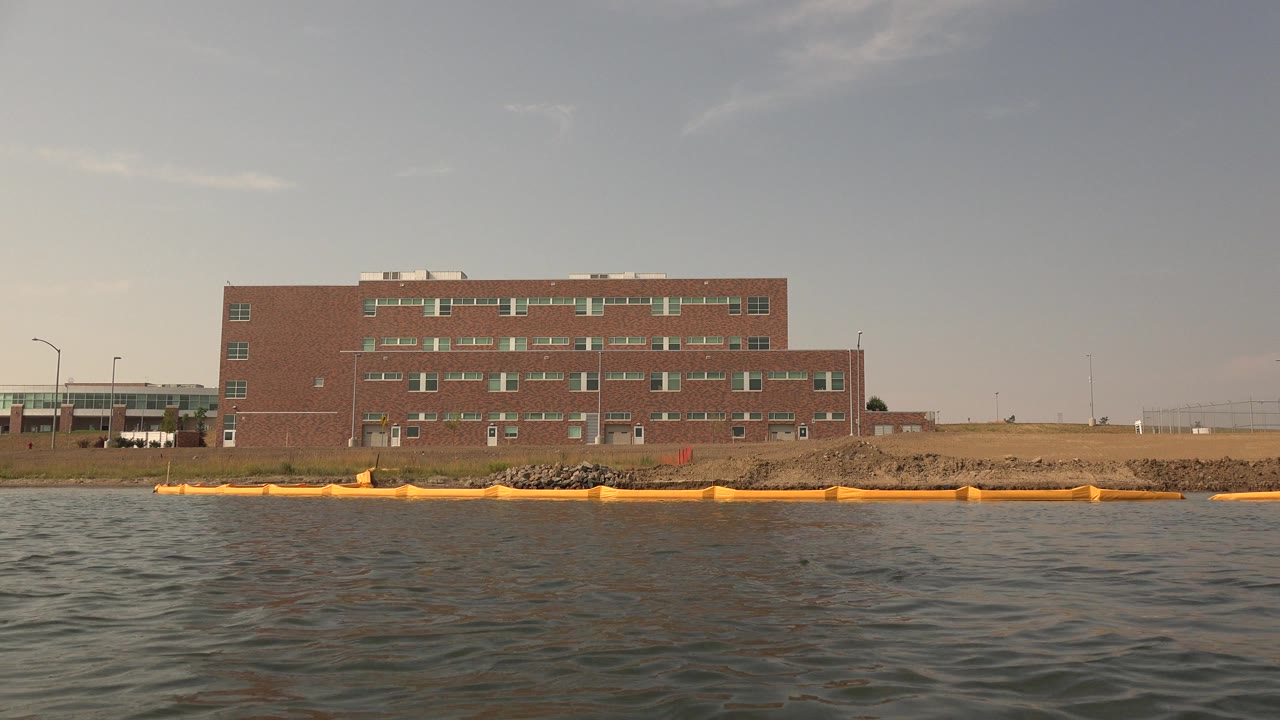 Lake water in front of a brick building and yellow shoreline barrier.