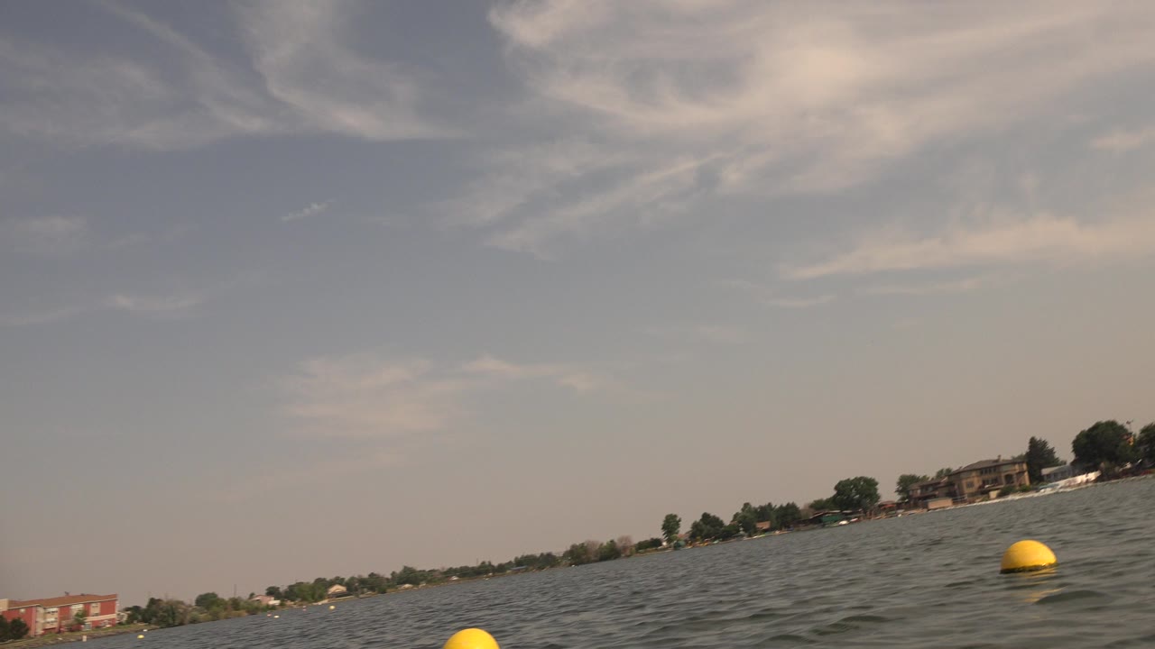 Tilted lake horizon with choppy water, yellow buoy, distant shoreline, and hazy sky.