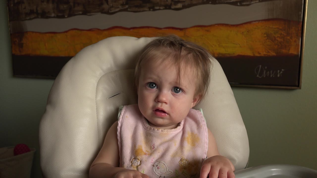 Baby in a pink bib seated in a white high chair