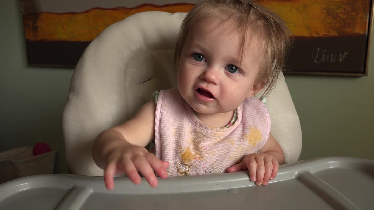 The toddler remains centered in the high chair at Hidden Lake, Colorado, reaching one hand forward over the tray while looking toward the camera.