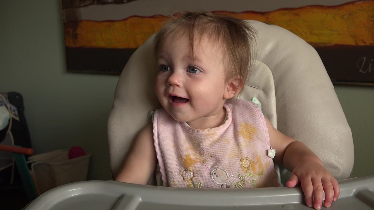 Young girl in a high chair looking left with her mouth open.