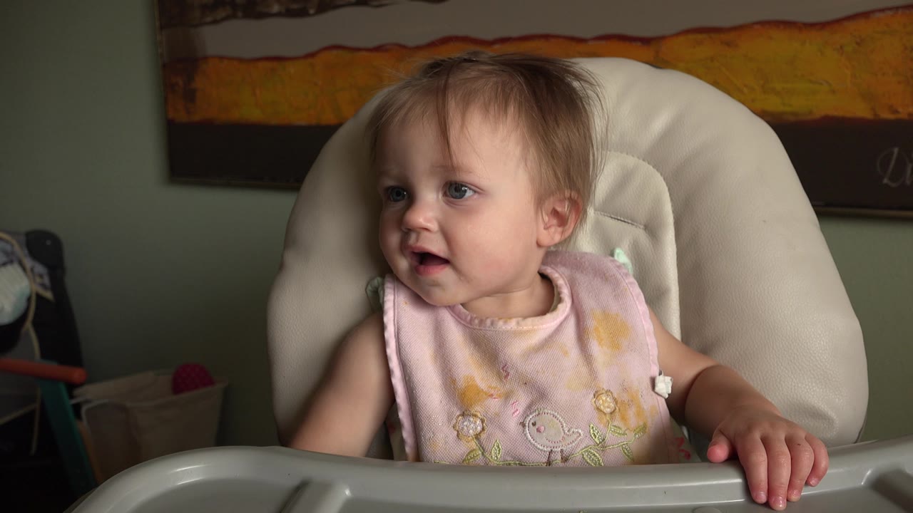 Young girl in a high chair turned slightly right with an attentive expression.