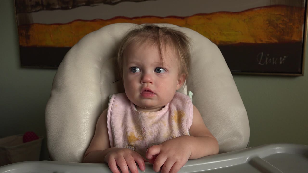 Blond baby seated in a high chair looking off to the side.