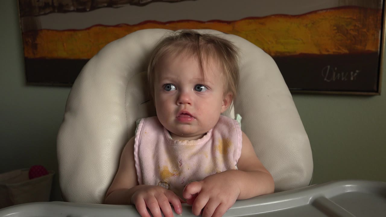 At 0:01, the baby remains seated in the high chair at Hidden Lake, Colorado, with both hands near the tray edge and eyes turned to the side.