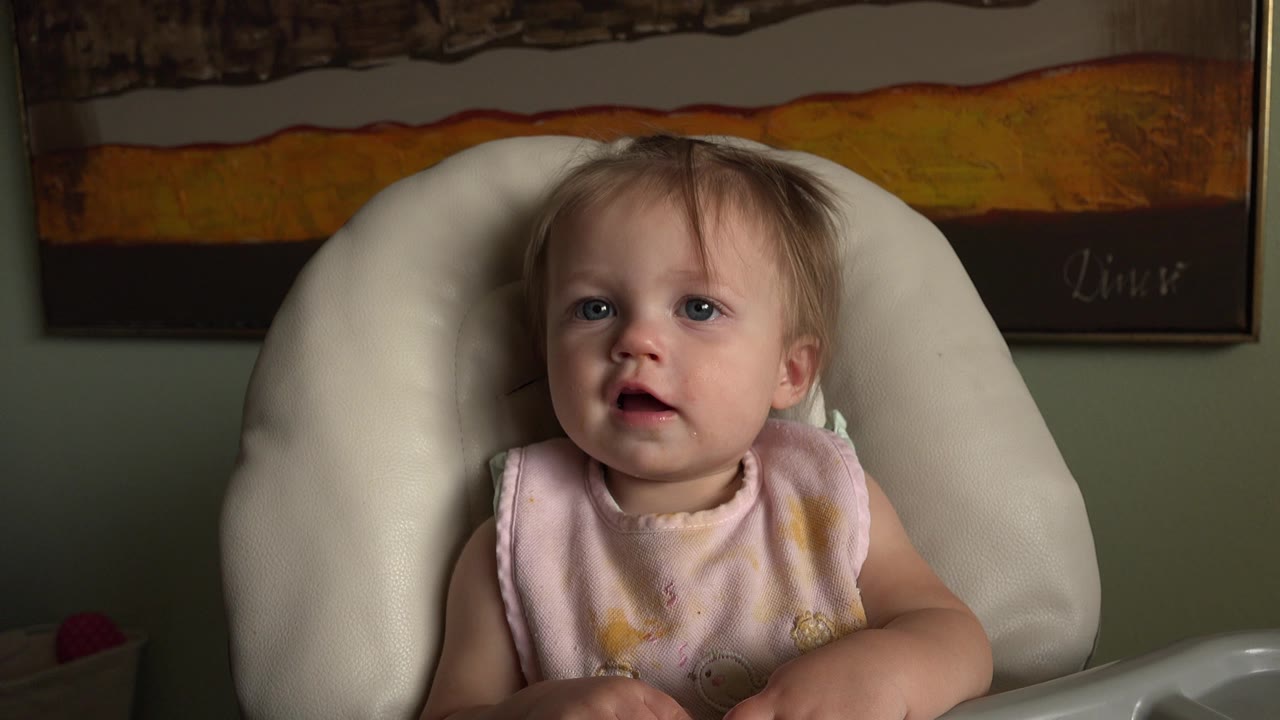 Toddler seated in a white high chair under soft side light.