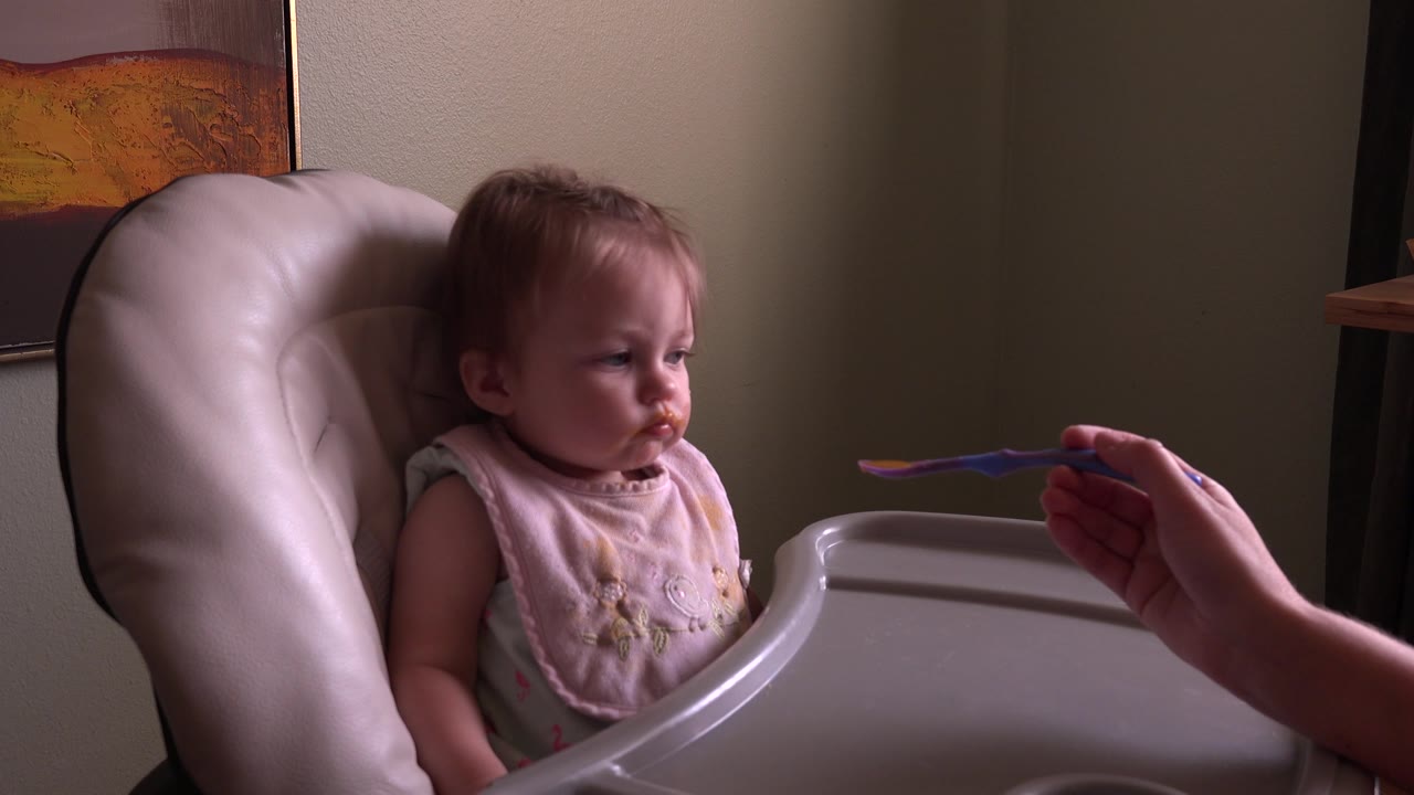 At Hidden Lake, Colorado, the baby stays seated in the high chair while the adult hand holds the spoon just short of the child's face.