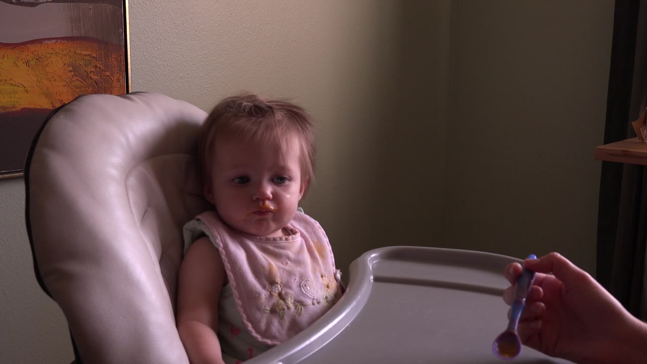 At 0:01, the baby remains seated in the padded high chair at Hidden Lake, Colorado while the spoon stays low near the tray in the right foreground.