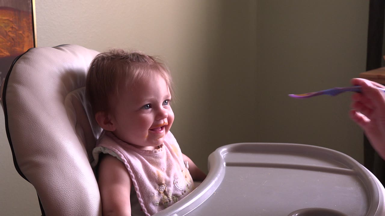 Baby smiling in a booster chair at a tray.