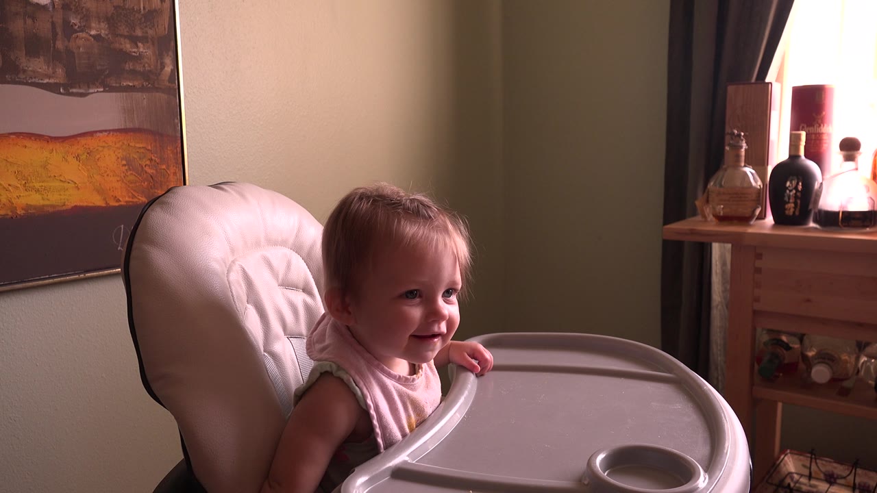 Baby girl in a high chair turning her face toward the right side of the room.