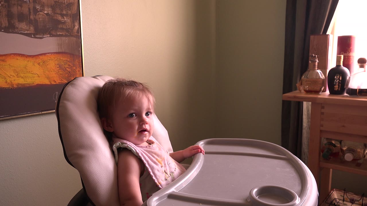 Baby seated in a booster chair beside a tray in a warmly lit room.