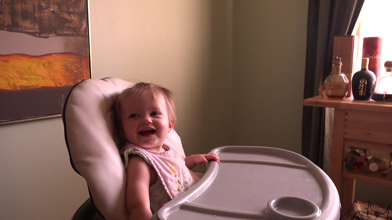 Smiling baby girl seated in a highchair indoors.