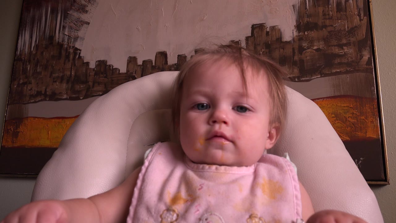 Toddler girl seated in a white chair indoors.