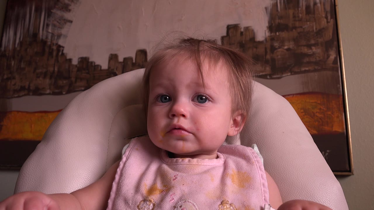 Baby in a high chair facing the camera with a pink bib.