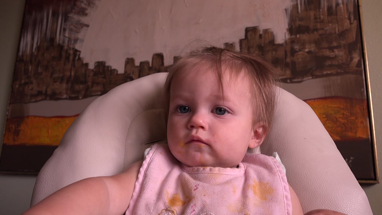A baby in a pale pink bib sits in a light-colored chair at Hidden Lake, Colorado, with framed abstract wall artwork behind them.