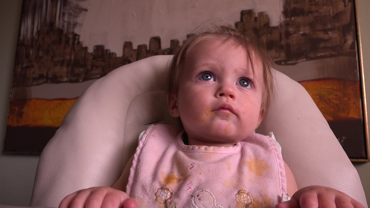 One second in, the baby remains centered in the padded seat, eyes lifted and mouth closed, with the warm-toned wall artwork behind the chair.
